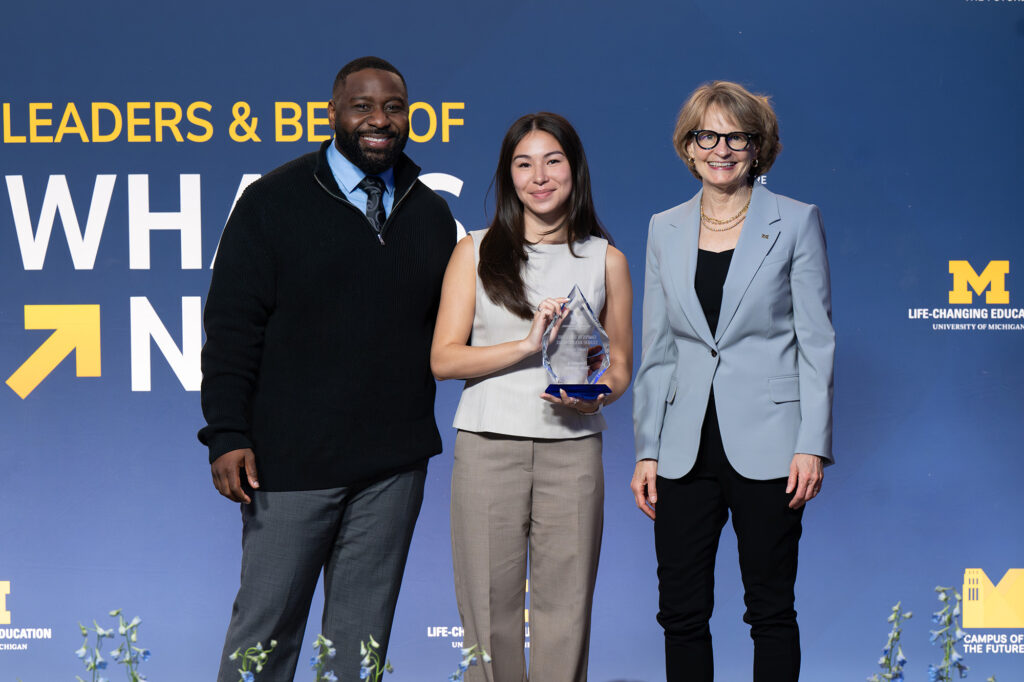 Three people stand together, with one holding a glass trophy