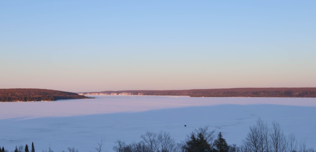 Lake Superior, covered in ice, at dusk. One lone ice fisher hut sits on the lake as night falls.