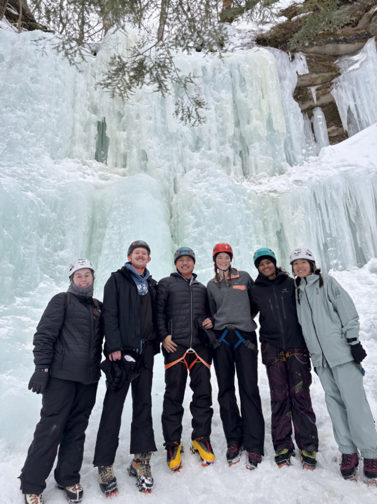 A team of School for Environment and Sustainability master's degree students stand in front of a frozen waterfall.