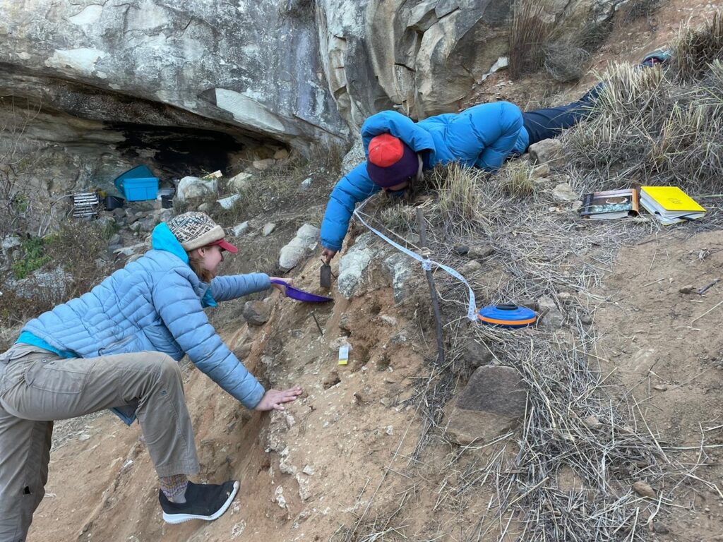 Kristin Cimmerer of University of Toronto, Mississauga, and Kyra Pazan of California State University, Stanislaus, excavate Likonong Rock Shelter in the mountains of Lesotho. Here, an international team of archaeologists from the United States, Canada, the United Kingdom, and Lesotho have identified the earliest sustained human occupation in Highland Southern Africa. Image credit: Kyra Pazan, California State University, Stanislaus