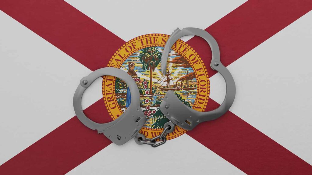 A half opened steel handcuff in center on top of the US state flag of Florida. Image credit: Adobe Stock